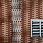 A close-up of a brown and beige brick wall featuring a white vent and geometric design.