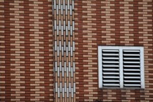 A close-up of a brown and beige brick wall featuring a white vent and geometric design.