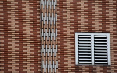 A close-up of a brown and beige brick wall featuring a white vent and geometric design.