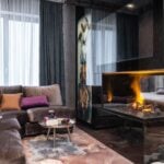 Interior of modern apartment with comfortable couch and side table with decorations placed near burning fireplace at bed