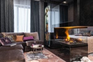 Interior of modern apartment with comfortable couch and side table with decorations placed near burning fireplace at bed