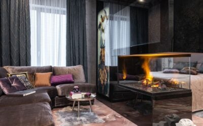 Interior of modern apartment with comfortable couch and side table with decorations placed near burning fireplace at bed