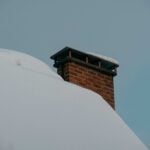 Brick chimney on a snow-covered roof, illustrating freeze-thaw chimney damage in Indiana