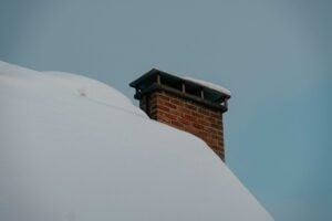 Brick chimney on a snow-covered roof, illustrating freeze-thaw chimney damage in Indiana
