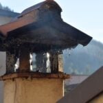 Close-up of a brick chimney stack releasing smoke, highlighting urban architecture.